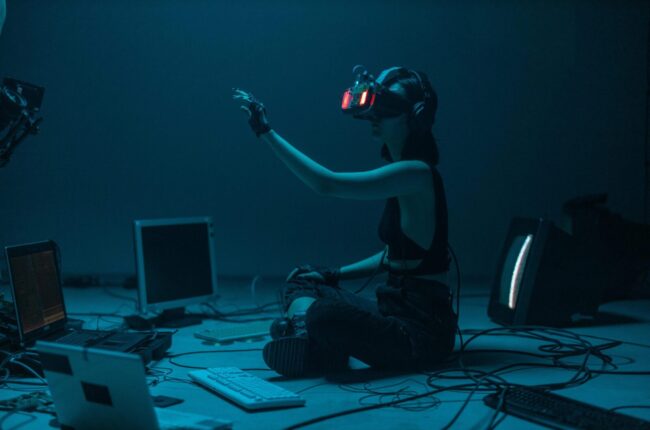 Woman immersed in virtual reality, surrounded by tech, in a dimly lit room.